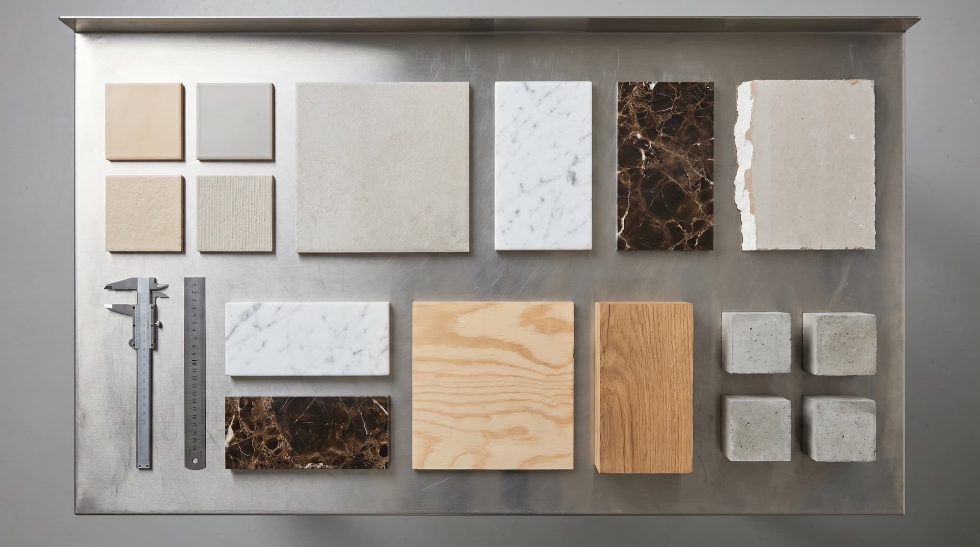 Flat lay of construction material test samples — tiles, marble, gypsum board, plywood, timber and concrete cubes on a laboratory bench